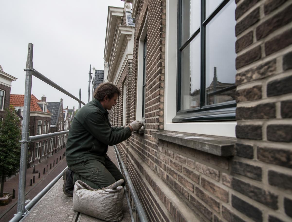 Vakmensen renoveren de bakstenen gevel van een Nederlandse rijwoning vanaf een steiger